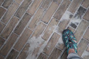 A gray and teal shoe standing on a street of wooden bricks
