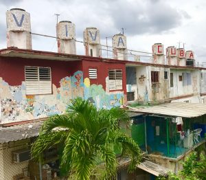 Eight cylindrical mosaics perched on top of a building. Each one contains a different letter so together they read "VIVA CUBA"
