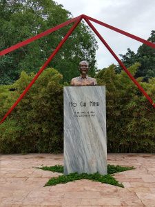 Bust of Ho Chi Minh on a rectangular pedestal with his birth and death dates written on it, beneath 4 red bars that intersect about it