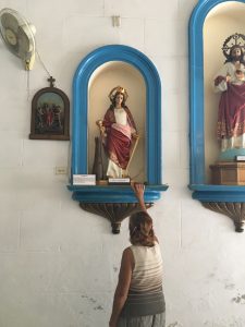 A woman reaches above her to touch the base of a figure of Santa Bárbara
