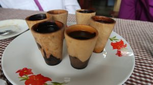 Small cups of coffee in wooden, handle-less cups rest on a white place decorated with red flowers