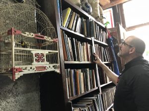 A man looks at shelves of books. A bird in a birdcage hangs in the foreground.