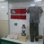 Museum display of a uniform, flag, lantern, plaque, and book