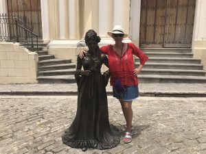 A woman stands next to the bronze statue of another woman